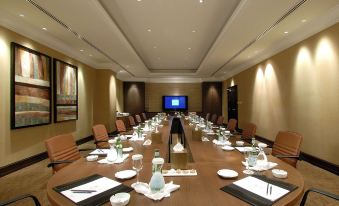 a conference room with a long wooden table , multiple chairs , and a television mounted on the wall at Djibouti Palace Kempinski