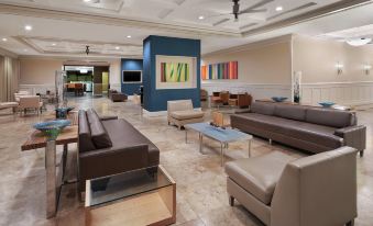a modern lounge area with multiple couches and chairs , a tv , and a painting on the wall at DoubleTree by Hilton Sunrise - Sawgrass Mills