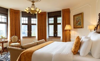 a large bed with white sheets and a gold throw is in the center of a room with brown curtains at Schloss Lieser, Autograph Collection