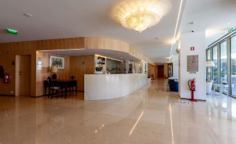 a modern office lobby with a marble floor , white reception desk , and large chandeliers hanging from the ceiling at Sea Porto Hotel