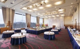 a large banquet hall with multiple tables set up for a formal event , including cakes , flowers , and other decorations at Hakodate-Onuma Prince Hotel