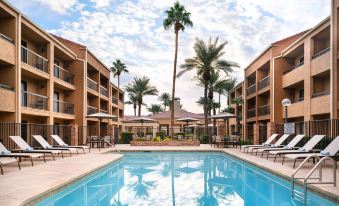 an outdoor pool surrounded by multiple buildings , with palm trees in the background and lounge chairs around the pool at Courtyard by Marriott Las Vegas Convention Center