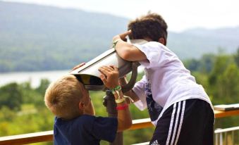 two young boys are playing with a telescope on a hill , looking out over a body of water at Nature Inn at Bald Eagle