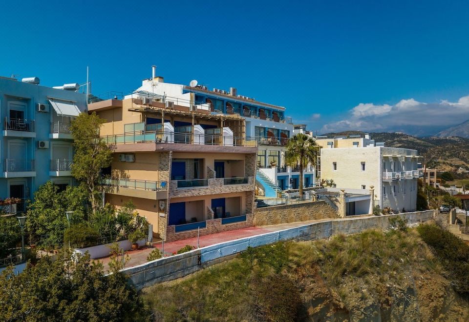 a large apartment building surrounded by trees and grass , located on the side of a hill at Minos Boutique Hotel