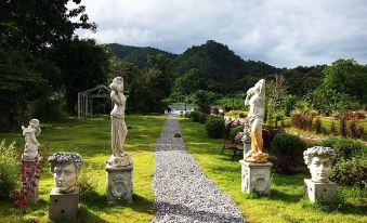 a garden path lined with stone statues leads to a grassy area with mountains in the background at Cinque Terre Resort