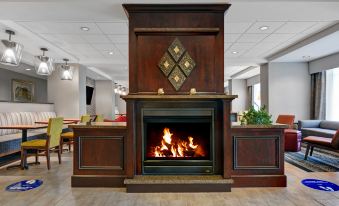 a large wooden fireplace with a fire burning inside it , surrounded by chairs and couches at Hampton Inn Bath (Brunswick Area)