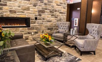 a cozy living room with a fireplace , two chairs , and a coffee table in front of it at Cobblestone Hotel & Suites - Chippewa Falls