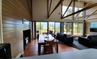 a spacious living room with wooden floors , a fireplace , and large windows overlooking the water at Waterfront Retreat at Wattle Point