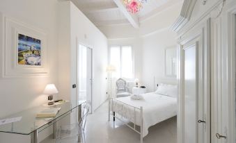 a white bedroom with a bed , a chair , and a chandelier hanging from the ceiling at Hotel San Giovanni