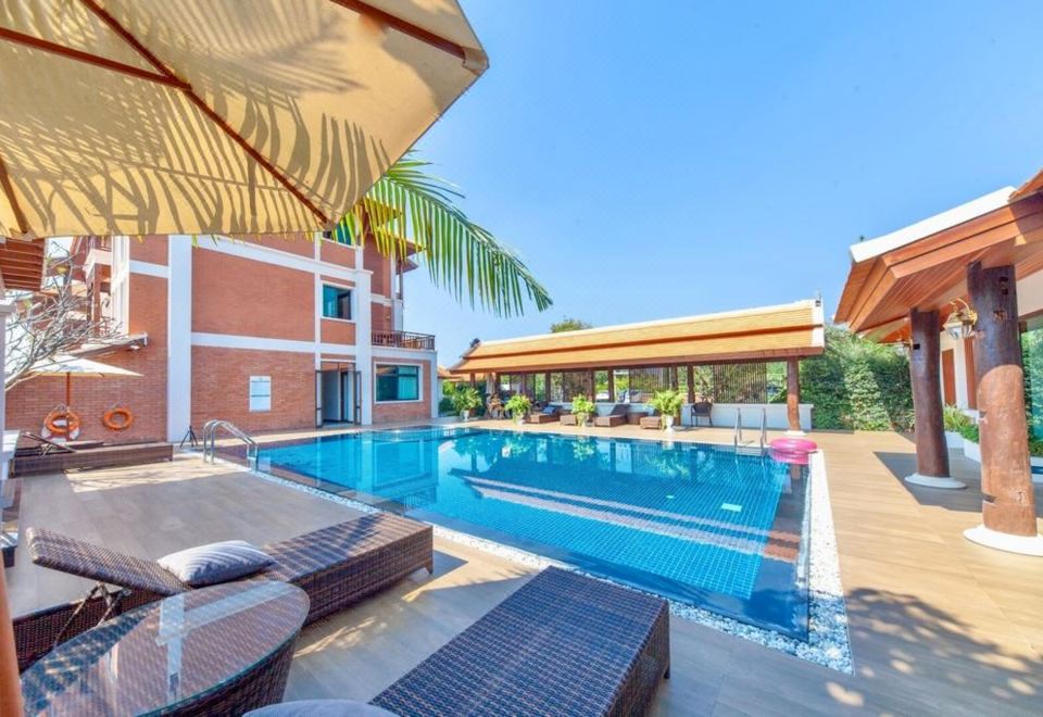 a large swimming pool is surrounded by lounge chairs and a red building with a thatched roof at Content Villa Chiangmai