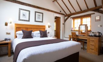 a large bed with a wooden headboard and white linens is in a room with a desk , chairs , and pictures on the wall at Tewinbury