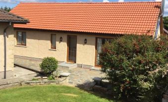 a house with a red tile roof and beige walls is surrounded by green grass and bushes at Burnside Cottage