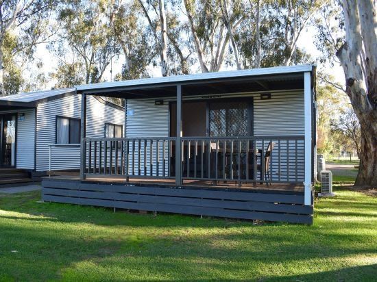 a small house with a deck and porch is surrounded by trees in a grassy area at Cohuna Waterfront Holiday Park