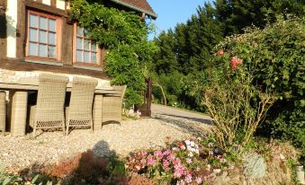 a house with a garden and outdoor seating area , surrounded by trees and flowers , under a clear blue sky at Le Pressoir