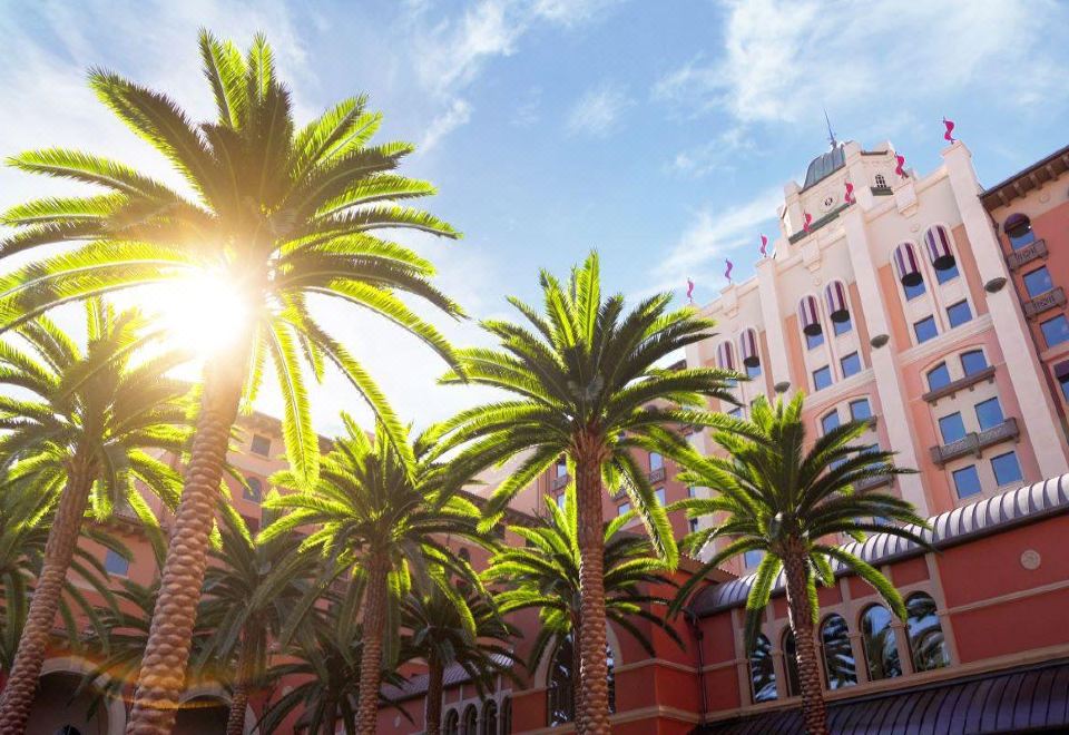 There is a group of trees in front of the main entrance to a tourist apartment building at The Universal Studios Grand Hotel