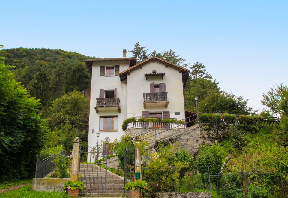 a white two - story house with a balcony and a staircase leading up to it , situated on a hillside at Gemma