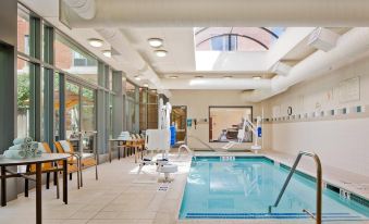 an indoor swimming pool with a diving board and chairs , surrounded by glass walls and tables at Courtyard by Marriott Boston Brookline