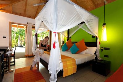 a woman and a child are standing next to a canopy bed in a hotel room at Vilamendhoo Island Resort & Spa