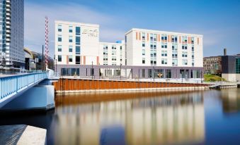 a modern , white and gray building with a reflection of the sky in a calm water body at Aloft Milwaukee Downtown