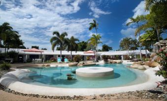 a large , circular pool with a white rock in the center surrounded by lounge chairs and umbrellas at Mission Beach Resort