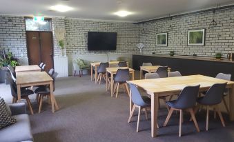 a room with several wooden tables and chairs , a television mounted on the wall , and a chalkboard at The Heritage Bendigo