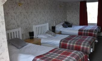 a bedroom with two beds , one of which has a plaid blanket and the other has a black headboard at The Gables