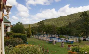 a large outdoor pool surrounded by lush green grass , with mountains in the background and blue skies above at Bestbrook Mountain Farmstay