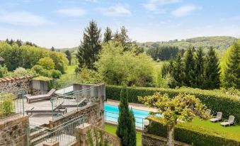 a large swimming pool is surrounded by a stone wall and trees , with a view of the countryside in the background at Auberge la Tomette, the Originals Relais