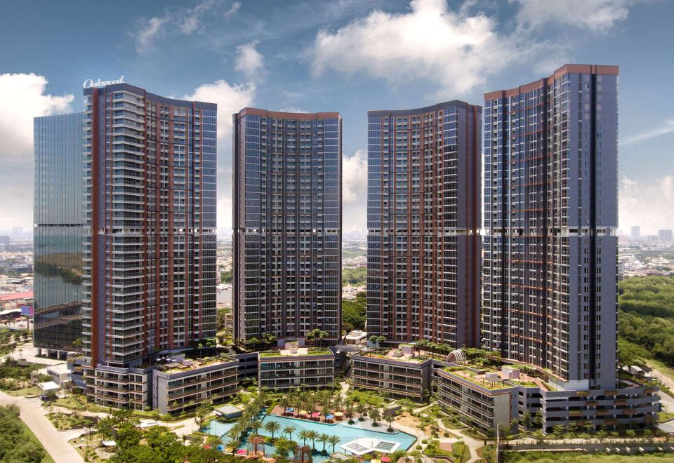 a group of tall , modern apartment buildings with a swimming pool in the foreground , surrounded by lush greenery at Oakwood Apartments Pik Jakarta