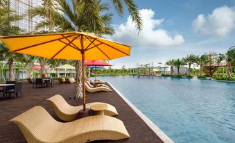 a large pool with a yellow umbrella and lounge chairs is surrounded by palm trees at Oakwood Apartments Pik Jakarta