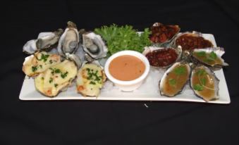 a white platter filled with a variety of oysters , accompanied by a dipping sauce and garnish at Streaky Bay Hotel Motel