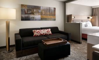a modern living room with a black leather couch , ottoman , and coffee table , along with a painting on the wall at Sonesta Select Seattle Renton Suites