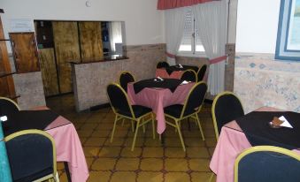 a room with pink tablecloths and chairs , a counter in the background , and a window with a curtain at Hotel San Francisco