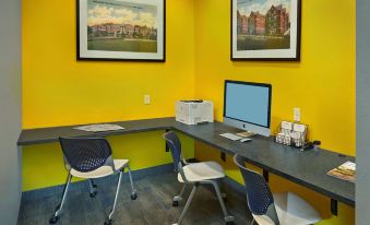 a desk with two computer monitors , a printer , and two chairs in a room with yellow walls at Scholar Morgantown, Tapestry Collection by Hilton