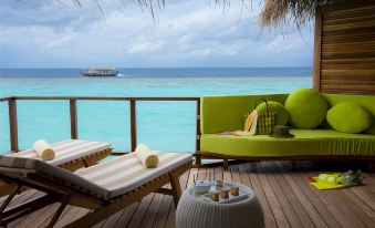 a tropical deck with two lounge chairs , a green sofa , and a table , offering a view of the ocean at Outrigger Maldives Maafushivaru Resort