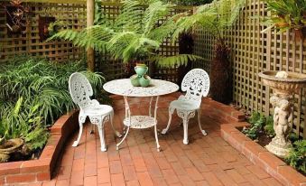 a small patio with a white table and two chairs surrounded by greenery , creating a serene and inviting atmosphere at Mary Cards Coach House