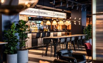 a modern bar with black and white chairs , a large number of bottles , and hanging lights at Scandic Falkoner