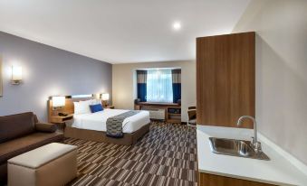 a modern hotel room with a bed , desk , and kitchenette , featuring carpeted flooring and gray walls at Microtel Inn & Suites by Wyndham Warsaw