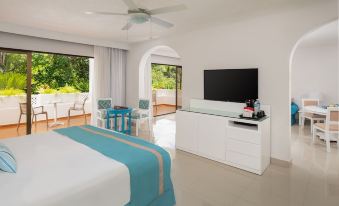 a white bedroom with a blue and white striped bedspread , a television , and a dining table at Sunscape Puerto Plata All Inclusive