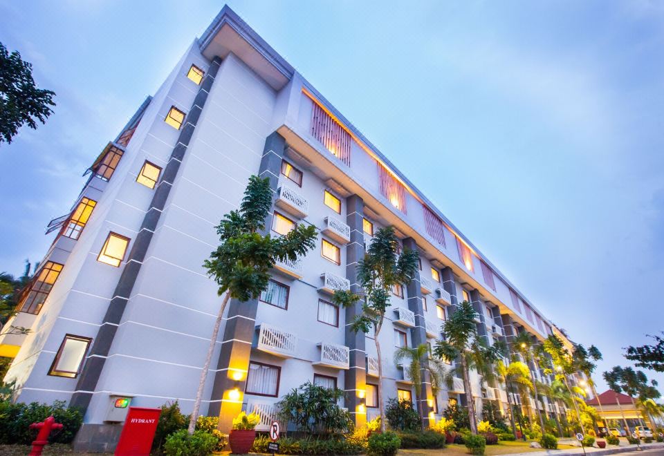 a large white building with many windows and balconies , surrounded by trees and plants , in front of a blue sky at Lorin Dwangsa Solo Hotel