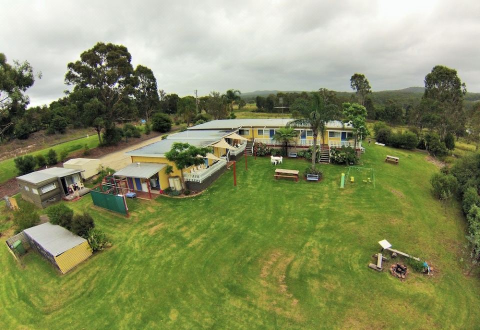 aerial view of a large yellow house surrounded by green grass and trees , with a playground nearby at Top of the Lake Holiday Units