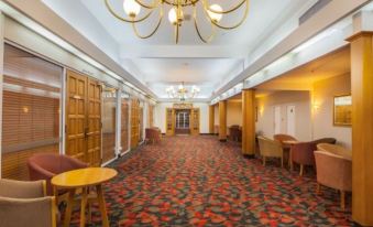 a large , empty hotel lobby with red carpet and gold chandeliers , wooden furniture , and a carpeted floor at Wairakei Resort Taupo