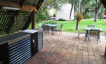 a brick patio with a grill , chairs , and tables is surrounded by trees and grass at A-Line Holiday Park