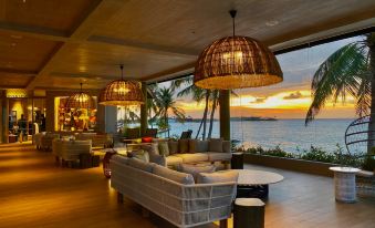 a spacious living room with a couch , chairs , and a dining table , overlooking the ocean at Hard Rock Hotel Maldives