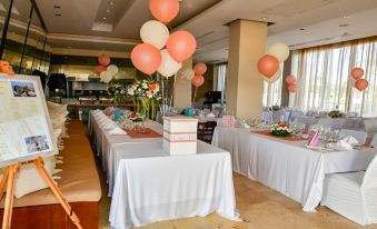 a dining room with multiple tables set up for a formal event , featuring white tablecloths and balloons at E-Hotel Larnaca Resort & Spa