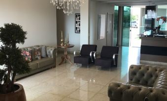 a modern living room with a large chandelier , green couches , and a potted plant , along with a reception area at Oasis Hotel