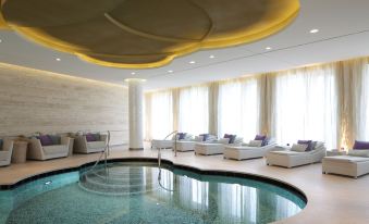 a large indoor swimming pool with a circular ceiling , surrounded by white sofas and cushions , under a curved ceiling with yellow light at Waldorf Astoria Berlin