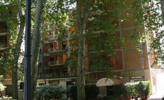 a brick building surrounded by trees , with a large tree in front of it , providing shade for the building at Hotel Mercurio