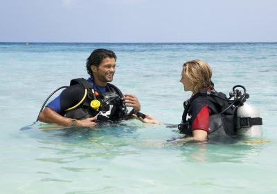 a man and a woman wearing scuba diving gear are in the ocean , with the woman standing in the water at Vilamendhoo Island Resort & Spa