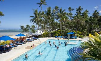 a large outdoor pool surrounded by palm trees , with several people enjoying their time in the water at Fiji Hideaway Resort and Spa